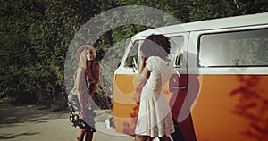 Two pretty girls making photo shoot on the road beside the vintage orange bus , happy dancing and smiling , wearing boho