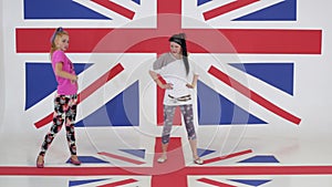 Two pretty girls practice synchronic dancing in room with wallpapers of UK flag