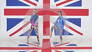 Two pretty girls synchronically dance and jump on background of british flag