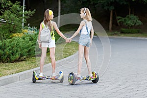 Two pretty happy girls riding on hover board or gyroscooter outdoors at sunset in summer. Active life concept