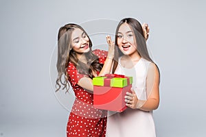 Two pretty happy young girls friends giving present box standing isolated over white background