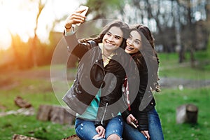 Two pretty and happy young woman using mobile phone in the park. Best friends make selfie.