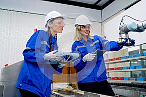 Two pretty professional technician or engineer women help to check the system use controller and ipad with robotic machine in