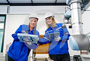 Two pretty professional technician or engineer women help to check the system use controller and ipad with robotic machine in