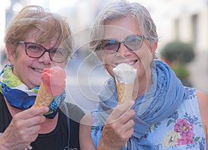 Two pretty senior women look at the camera and smile with an ice cream cone in their hands. Couple of people enjoying sweet food