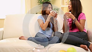 Two pretty sisters sitting on couch holding mugs