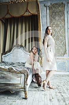 Two pretty twin sister blond curly hairstyle girl in luxury house interior together, rich young people concept