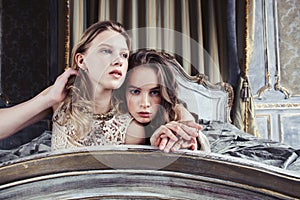 Two pretty twin sister blond curly hairstyle girl in luxury house interior together, rich young people concept