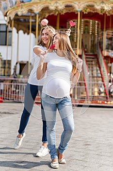 Two pretty women in amusement park having fun and eating sweets, happy family. Samesex lesbian family, pregnant couple.