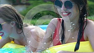 Two pretty women having fun in swimming pool, splashing water at each other