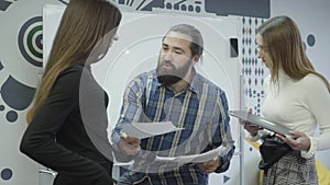 Two pretty women standing and communicating in the office. Bearded man on his bike riding closer and gives papers to