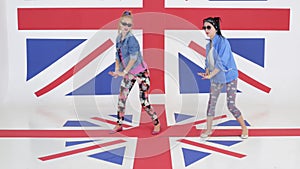 Two pretty women synchronically dance and jump on background of british flag