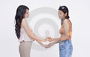 Two pretty and young asian women reaffirming their friendship, holding hands. Isolated on a white background