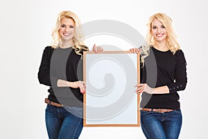 Two pretty young blonde sisters twins holding blank board