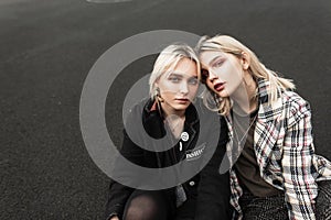 Two pretty young girlfriend blondes in stylish clothes with sexy lips relaxes on ashphalt outdoors. Portrait urban fine modern photo