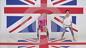 Two pretty young women are synchronically dancing on background of british flag