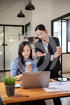 Two professional Asian businesswomen are working and examining a project on the laptop