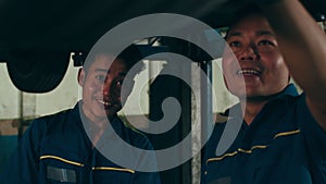 Two professional car mechanic using paperwork makes the oil and engine check to the car on lifted automobile at repair service