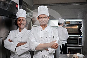 Two professional chefs in uniforms crossed arms and smiled in the kitchen