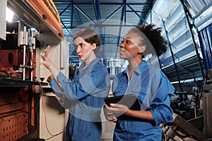 Two professional female engineers inspect machines` electric systems at factory