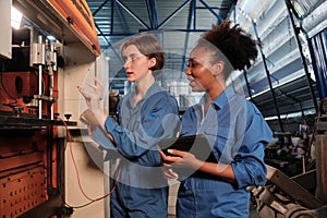 Two professional female engineers inspect machines` electric systems at factory