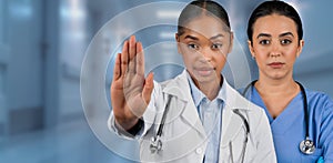 Two professional female healthcare workers, one in a white lab coat gesturing stop