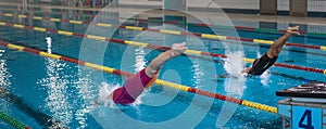 Two female swimmers taking the start position and jumping in a pool