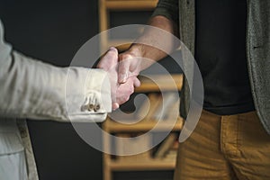 Two professional men engage in firm handshake in office, symbolizing agreement, collaboration, and trust. This gesture