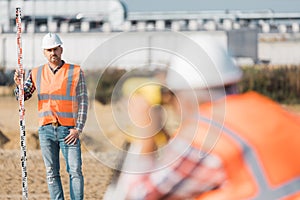 Two professional road construction workers in orange vests and protective helmets in the middle on the terrain