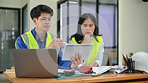 Two professional and serious Asian engineers are looking at a tablet screen, discussing work