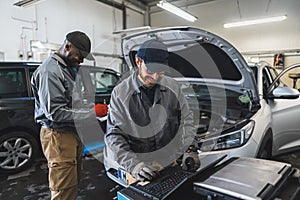 two professional servicemen making car diagnostics on a laptop and smiling, medium shot car repair shop