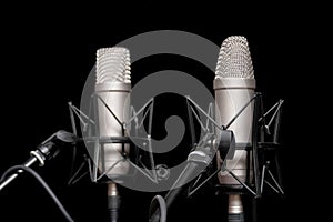 Two professional silver studio microphones on stands on black background, podcasting, voiceover. Interview or sports event