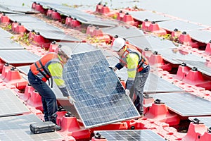 Two professional technician workers hold and carry solar cell panel to set up or install to the base over area of water reservoir