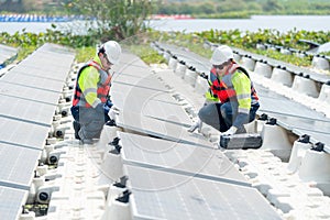 Two professional technician workers sit on footpath of row of solar cell panels and check or maintenance in area of green energy