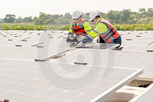 Two professional technician workers sit and work together and work with solar cell panel on base over water reservoir