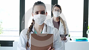 Two professional young females doctor wearing a hygienic facial mask looking at camera standing in the hospital.