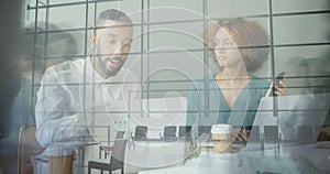 Two professionals collaborating at conference table, with laptops and grid reflection on glass wall