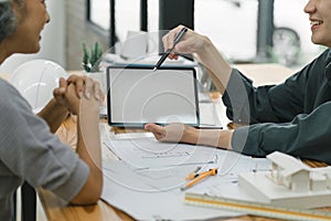 Two professionals engaged in a detailed discussion over a digital tablet, with architectural plans and a model house on