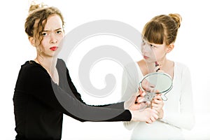 Two puberty girls in black and white dresses haggle to get a mirror to make a make up - sister rivalry