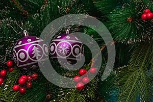 Two purple festive balloons with the image of a Christmas tree and snowflakes hanging on artificial branches of a spruce