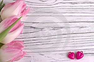 Two purple hearts with rose tulips on white painted rustic white wooden background. Valentine Day.