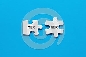 Two puzzle pieces are connecting the word merger. Company merger and acquisitions in business photo