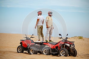 Two racers in helmets stand back to back on atvs