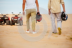 Two racers hold helmets near atvs in desert