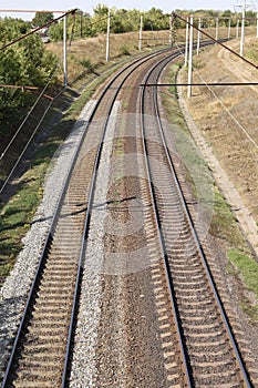 Two railroad tracks lie on a crushed rock railroad bank and lead to the right into the woods. Top view