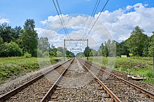 Two railway tracks with electric power cables into the distance in the middle of a green forest, the Netherlands