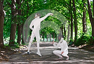 Two rapier fencer women fighting over park alley