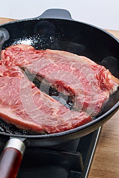 Two raw beef steak fried in a cast iron skillet