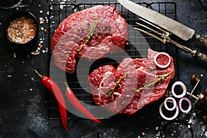 Two Raw beef steak with spices, onions and chili on dark slate or concrete background.