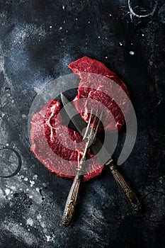 Two Raw beef steak with spices, onions and chili on dark slate or concrete background.